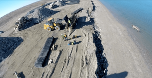 aerial view of a clear shoreline with riprap stones ready to be placed behind a construction vehicle